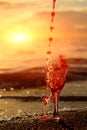 Romantic beach scene: glass of red wine at sunset near water line with splashes Royalty Free Stock Photo