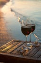 Romantic beach scene: two glasses of red wine at sunset near water