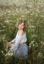 Romantic beautiful young woman sits among a field of wild white daisies