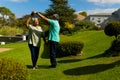 Romantic biracial senior couple holding hands and dancing in park against sky during sunny day Royalty Free Stock Photo