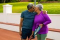 Romantic biracial senior husband and wife holding rackets and kissing while standing in tennis court Royalty Free Stock Photo