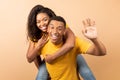 Romantic black couple having fun together, man waving at camera and piggybacking his girlfriend over peach background Royalty Free Stock Photo