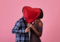 Romantic black couple kissing behind heart shaped balloon on Valentine`s Day over pink studio background, side view Royalty Free Stock Photo