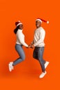 Romantic Black Couple In Santa Hats Holding Hands And Jumping, Orange Background Royalty Free Stock Photo