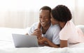 Romantic black man and woman using laptop in bed