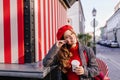 Romantic blue-eyed woman in beret dreamy posing with cup of coffee. Outdoor portrait of graceful curly lady tasting