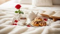 Romantic breakfast in bed with tea, cinnamon rolls, and a book on a cozy white comforter Royalty Free Stock Photo