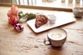 Romantic breakfast, Valentine`s Day celebrating. Present box, rose flowers, fresh croissant, coffee on wooden table. Focus on cup.