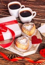 Romantic breakfast for Valentine`s Day. Two cups of coffee, cupcakes in the form of a heart on a white board on a wooden table,