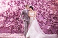 Romantic bridegroom kissing bride on forehead while standing against wall covered with pink flowers Royalty Free Stock Photo