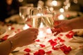 A romantic candlelit dinner: two clinking champagne glasses, table adorned with rose petals, warm candlelight fostering Royalty Free Stock Photo