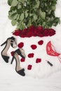 Romantic carnival concept. Red carnival mask, a bouquet of red roses, black shoes with heels, lipstick and scattered petals on