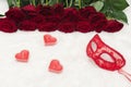 Romantic carnival concept. A red carnival mask and a bouquet of red roses and a heart-shaped candle on white fur