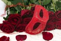 Romantic carnival concept. Red carnival mask and bouquet of red roses on light wooden background. Close-up