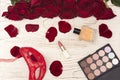 Romantic carnival concept. Red carnival mask, bouquet of red roses, lipstick, bottle of perfume and eye shadow on light wooden