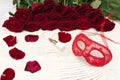 Romantic carnival concept. Red carnival mask, bouquet of red roses and lipstick on light wooden background
