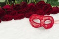Romantic carnival concept. Red carnival mask and a bouquet of red roses on white fur. Close-up
