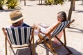 Romantic caucasian senior couple holding hands and sitting on deck chairs at sandy beach, copy space Royalty Free Stock Photo