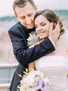 Romantic close-up portrait. Groom is hugging the bride back while stroking her cheek.