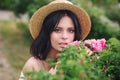 Romantic close-up portrait o charming brunette girl in straw hat smells flowers in rose bushes Royalty Free Stock Photo