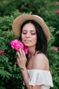 Romantic close-up portrait o charming brunette girl in straw hat smells flowers in rose bushes