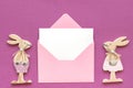 Romantic composition Pair of wooden lovers figurine rabbits and pink envelope with blank card on purple background Concept