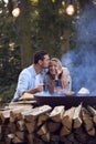 Romantic Couple Camping Sitting By Bonfire In Fire Bowl With Hot Drinks