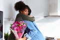 Romantic couple at home with man surprising woman with bunch of flowers celebrating valentines day, birthday or anniversary and