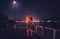 Romantic couple are kissing in the embankment of lake at night and lights of city on the background. Married couple of Royalty Free Stock Photo