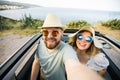 Romantic couple making selfie on smartphone camera in rental cabrio car on ocean or sea beach enjoying summer vacation together Royalty Free Stock Photo