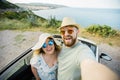 Romantic couple making selfie on smartphone camera in rental cabrio car on ocean or sea beach enjoying summer vacation Royalty Free Stock Photo