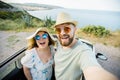 Romantic couple making selfie on smartphone camera in rental cabrio car on ocean or sea beach enjoying summer vacation Royalty Free Stock Photo