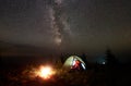 Young couple hikers resting near illuminated tent, camping in mountains at night under starry sky Royalty Free Stock Photo