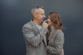 Romantic couple, mature gray haired man and young woman hugging, smiling and touching nose against gray wall outdoors Royalty Free Stock Photo
