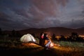 Romantic couple sitting by bonfire under cloudy sky