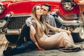 A romantic couple is sitting near red car. A man is hugging a woman. American classics. The guy and the girl next to the red car. Royalty Free Stock Photo