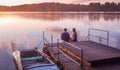 Romantic couple sitting pier golden sunset. Beautiful nature lake. man woman meet sunset. Beautiful couple outdoors near water Royalty Free Stock Photo