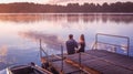 Romantic couple sitting pier golden sunset stroking dog. Beautiful nature lake. man woman meet sunset. Beautiful couple outdoors n Royalty Free Stock Photo