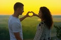 Romantic couple at sunset show a heart shape from hands, beautiful landscape and bright yellow sky, love tenderness concept, young Royalty Free Stock Photo