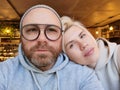 Romantic couple taking selfie in cafe. Young man in eyeglasses with blond woman. Royalty Free Stock Photo