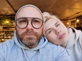 Romantic couple taking selfie in cafe. Young man in eyeglasses with blond woman. Royalty Free Stock Photo