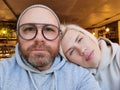 Romantic couple taking selfie in cafe. Young man in eyeglasses with blond woman. Royalty Free Stock Photo