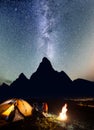 Romantic couple tourists sitting face to face in front tent near bonfire under shines starry sky at night