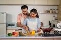 Romantic couples preparing food by slicing vegetables at kitchen while preparing food by hugging - concept of