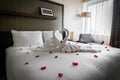 Romantic cozy boutique hotel room getaway with gorgeous swan towels red rose and petals spread on the bed waiting for valentine Royalty Free Stock Photo