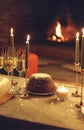 Romantic cozy photo of festive dinner table set with freshly baked Christmas cake against fireplace Royalty Free Stock Photo