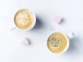 Romantic desk top with two cups of coffee and pink heart shaped marshmallows. Top view.