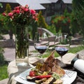 Romantic dinner outside. an appetizing dish of pork ribs and two glasses of red wine, green grass and flowers in the background.