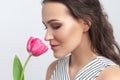 Romantic dreaming brunette woman standing holding pink tulip, enjoying aromat of flower.