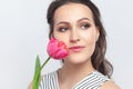 Romantic dreaming brunette woman standing looking away, holding pink tulip enjoying aromat of flower